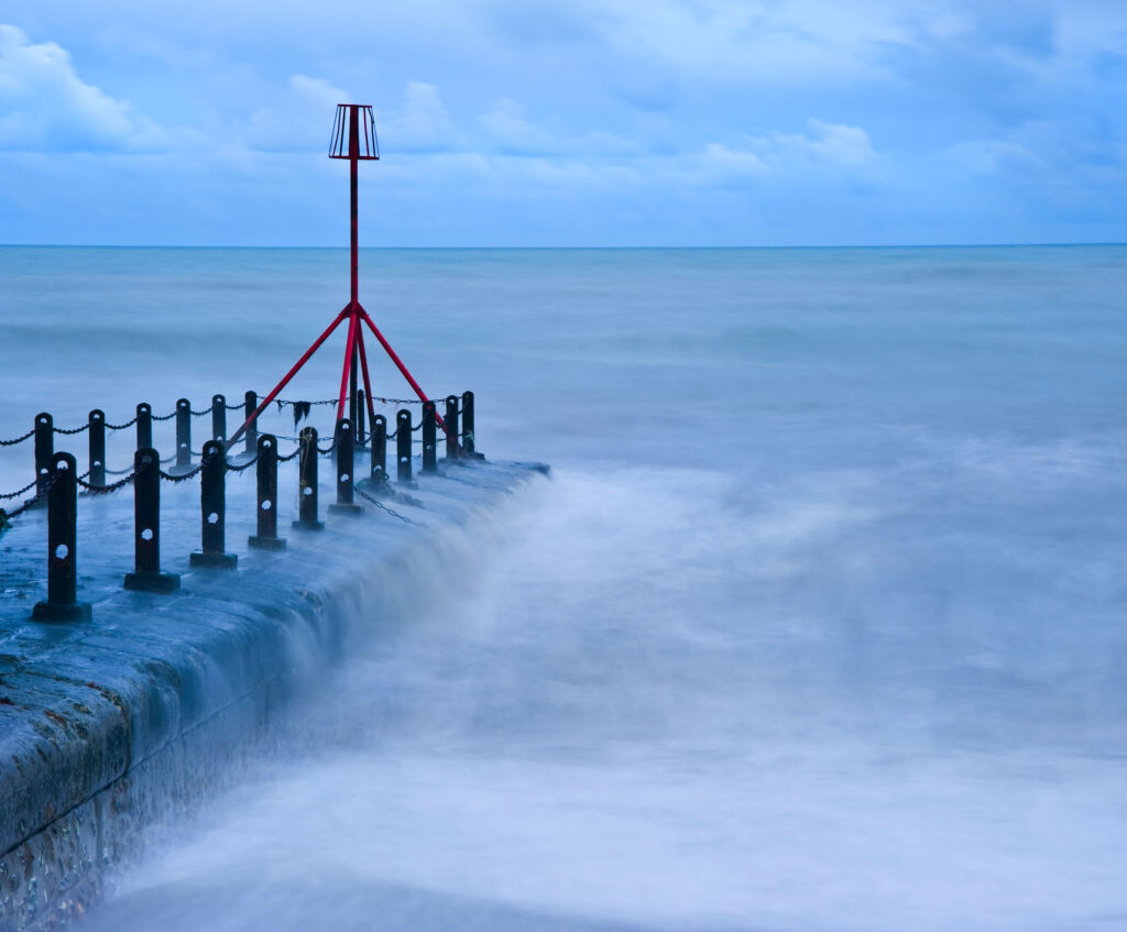 A stormy pontoon with waves crashing against the stone under a grey sky.