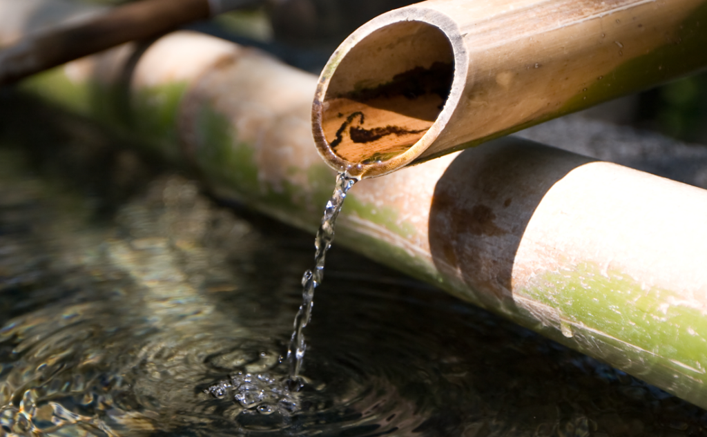 A bamboo spout releases clear water into a tranquil pond.