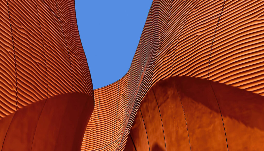 Orange textured curved building against a clear blue sky.
