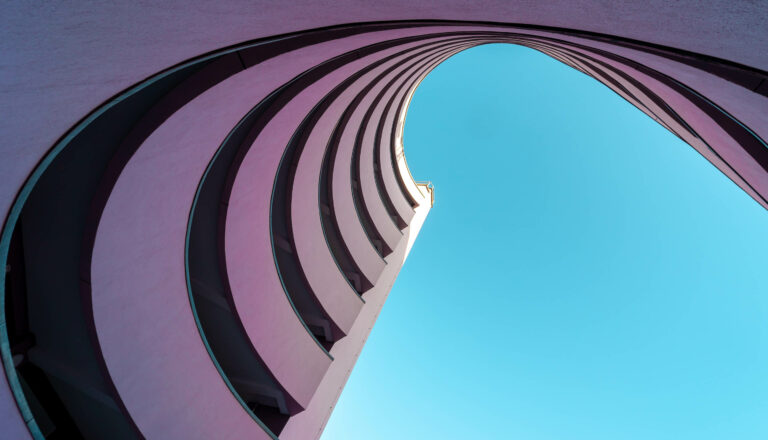 A unique architectural view of curved, layered structures against a bright blue sky, framed from below.