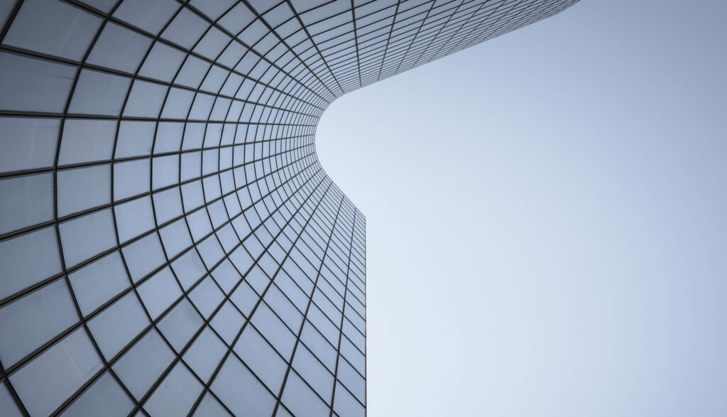View of a modern, curved glass building with a sleek design, captured from below against a clear sky.