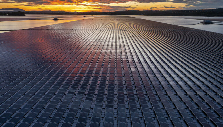 Solar panel farm at sunrise next to a reservoir.