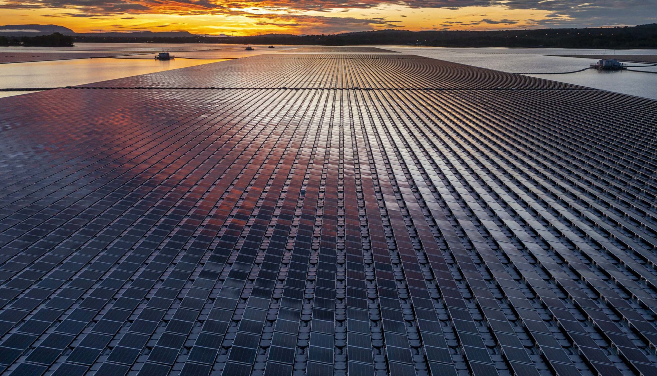 Solar panel farm at sunrise next to a reservoir.