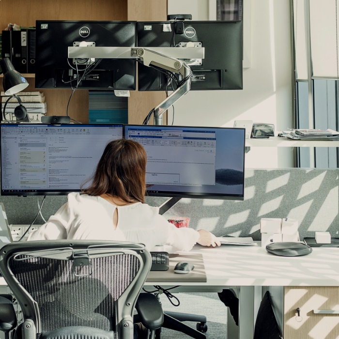 A woman works at a desk working on dual monitors.