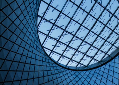 Geometric glass ceiling with a circle opening showcasing a blue sky.